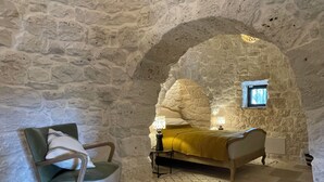 A room with a stone wall, a bed with a yellow blanket, a chair, and a small window. - Casa Pampini. A stunning villa set in beautiful Valle d’Itria with private pool (Ceglie Messapica)
