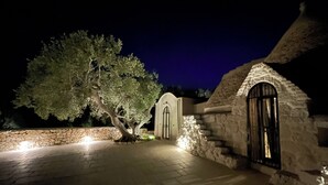 A stone building with a large tree in front, a paved entrance, and a lit door. - Casa Pampini. A stunning villa set in beautiful Valle d’Itria with private pool (Ceglie Messapica)