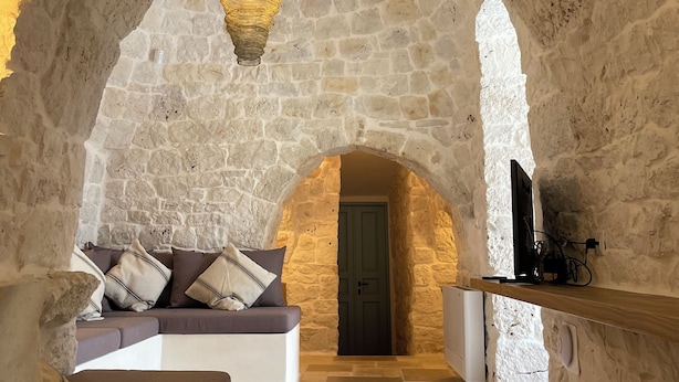 A cozy stone-walled room with a sofa, a decorative hanging light, and a television on a wooden shelf. - Casa Pampini. A stunning villa set in beautiful Valle d’Itria with private pool (Ceglie Messapica)