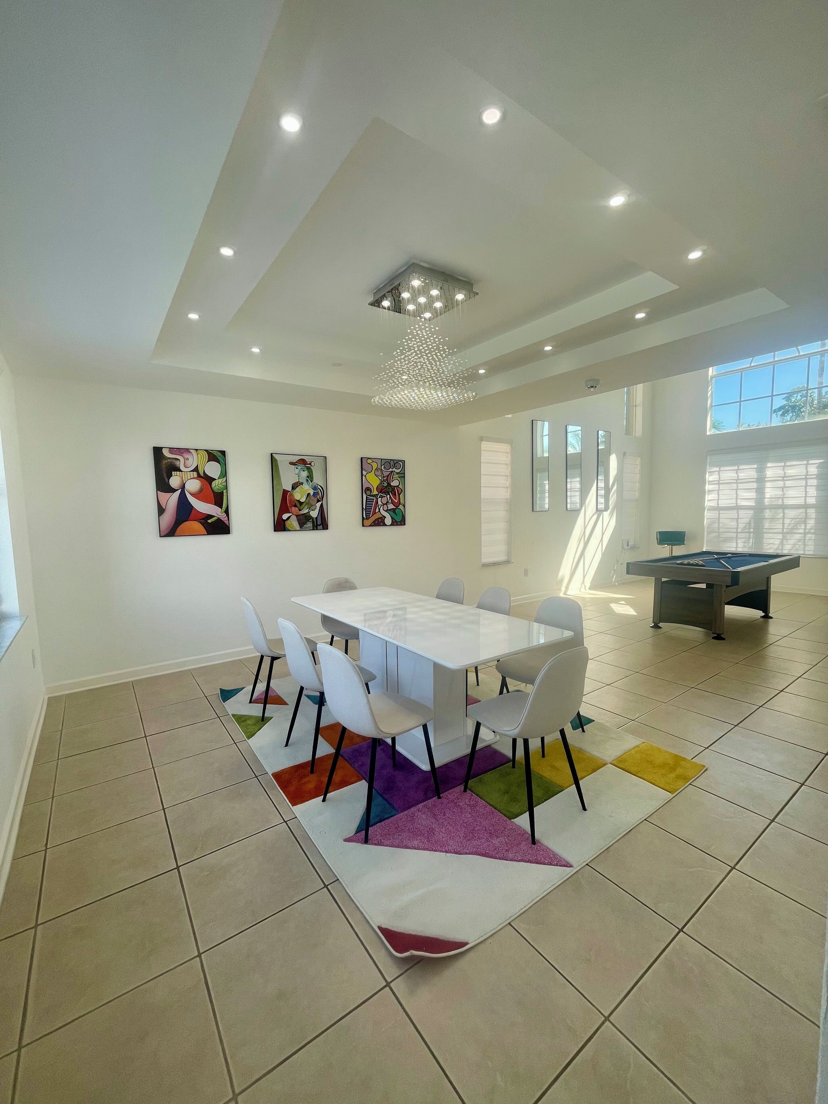 Un espace repas moderne avec une table et des chaises blanches, des tapis colorés et des œuvres d’art abstraites accrochées aux murs.