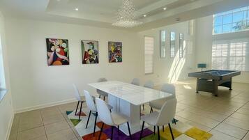 Un espace repas moderne avec une table et des chaises blanches, des tapis colorés et des œuvres d’art abstraites accrochées aux murs.