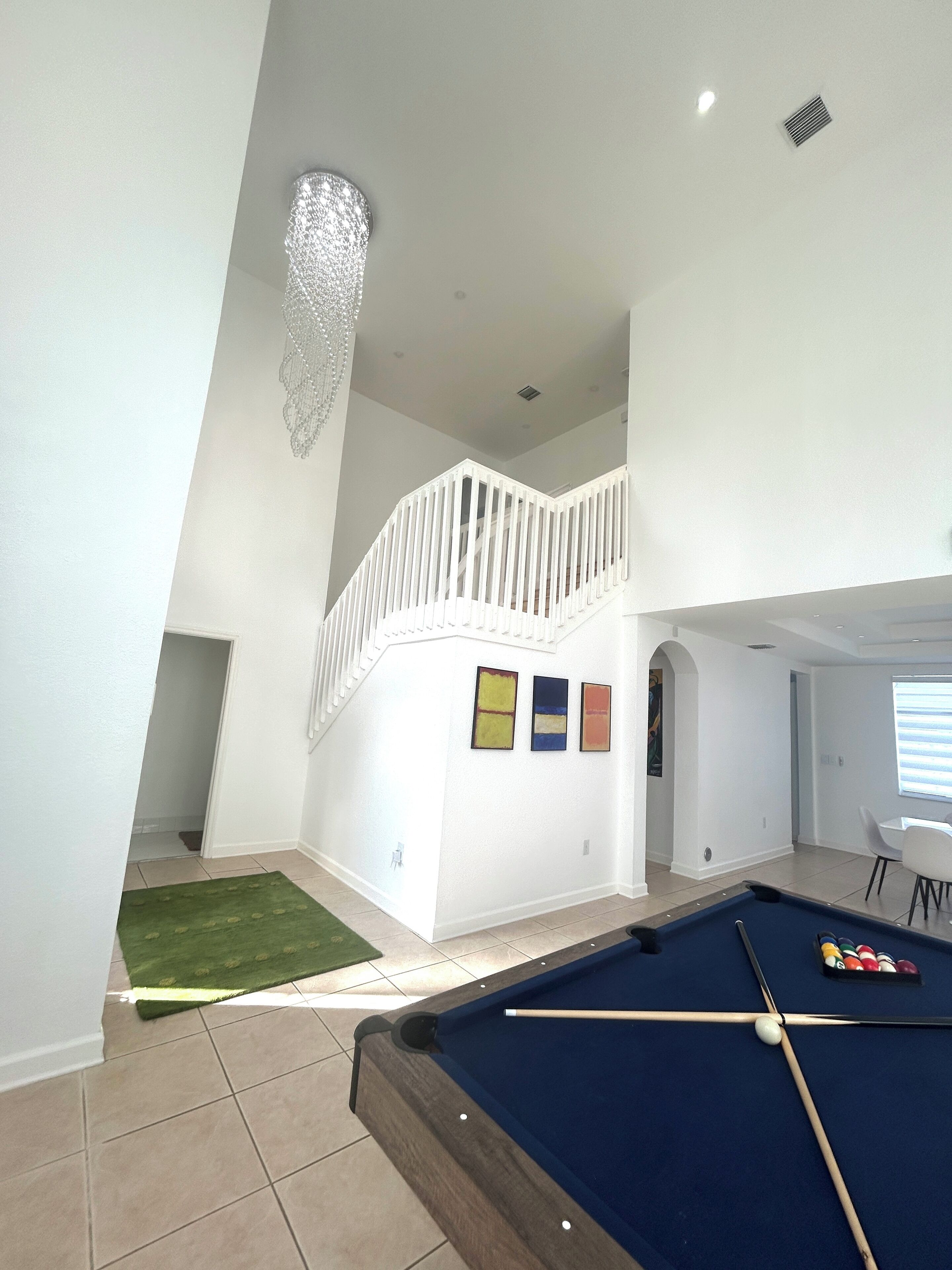 Un vaste espace intérieur comprenant une table de billard, un escalier menant à un niveau supérieur et un lustre.