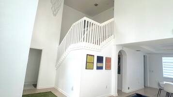 Un vaste espace intérieur comprenant une table de billard, un escalier menant à un niveau supérieur et un lustre.