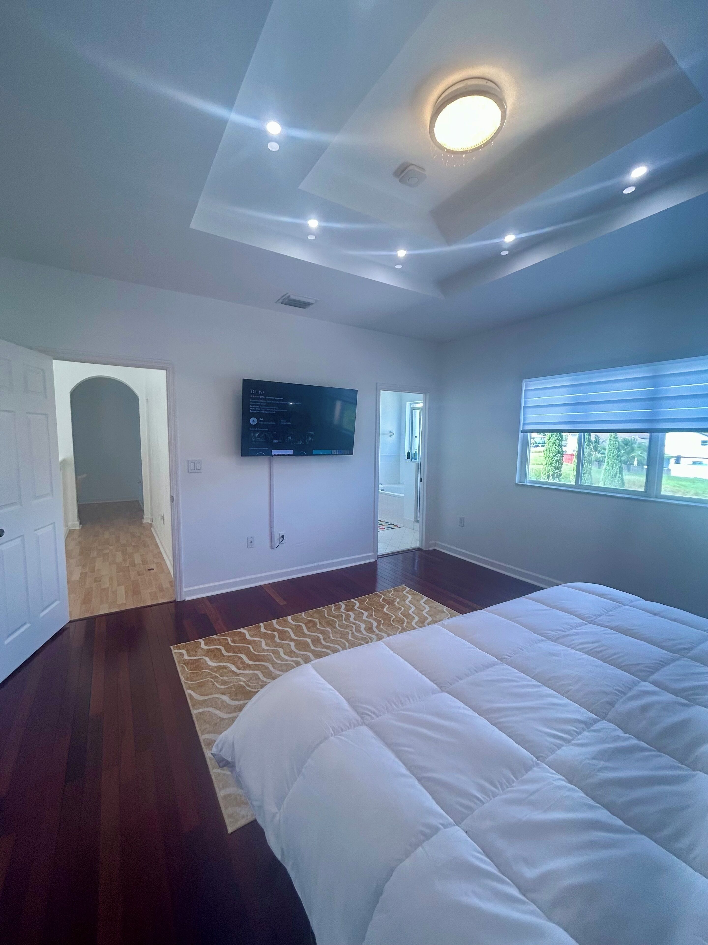Una camera da letto con un letto grande, una TV fissata al muro e una finestra con tende.
