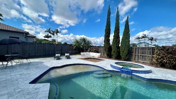 Un jardin avec une piscine, des meubles de jardin et de grands arbres.