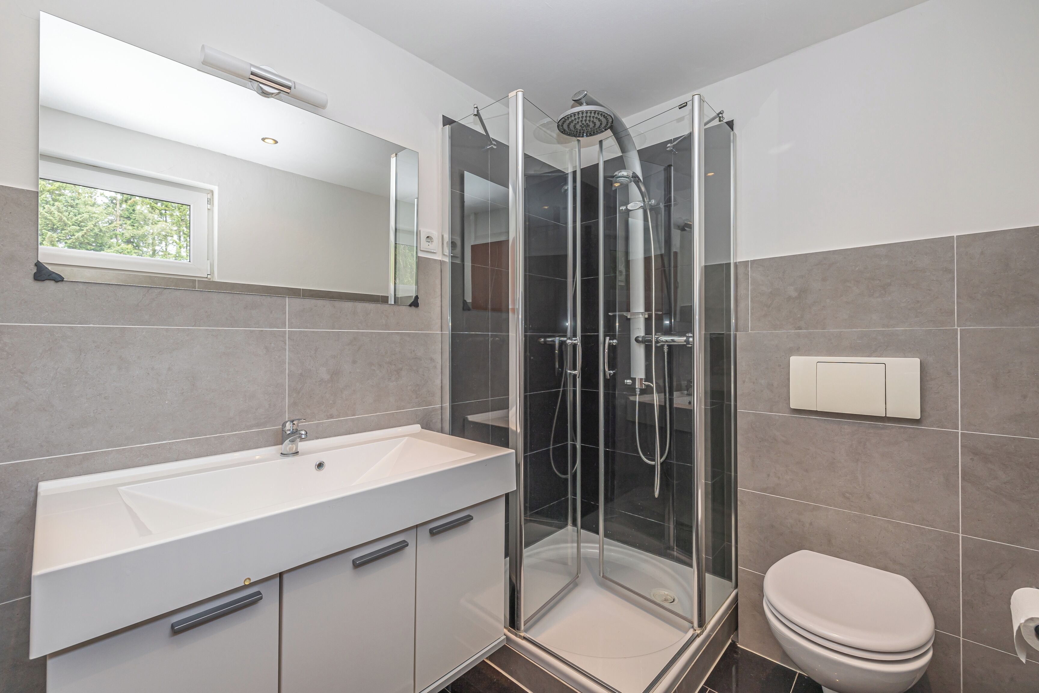 Een moderne badkamer met een douchekabine van glas, een witte wastafel en een toilet.