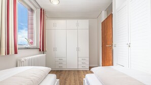 A bedroom with two beds, a window with curtains, a radiator, and a wardrobe.
