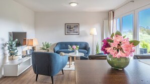 A modern living room with a blue sofa, a small round table, and a vase of flowers.