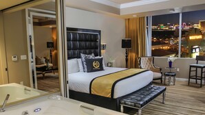 A hotel room with a large bed, a sitting area with a chair and a small table, a large window with a city view, and a separate bathroom with a bathtub and sink. - Westgate Resort & Casino Las Vegas 1-bedroom (Las Vegas)