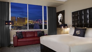 A hotel room with a large bed, a red leather sofa, a city view, and a framed artwork on the wall. - Westgate Resort & Casino Las Vegas 1-bedroom (Las Vegas)