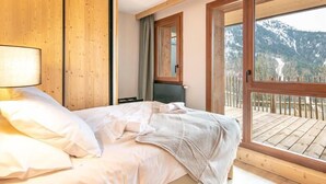 Un dormitorio con cama, paredes de madera, una ventana con vistas a la montaña y un balcón.