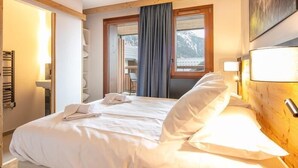 A hotel room with a bed, a window with a view of mountains, a wooden headboard, and a painting on the wall.