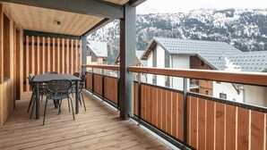 A wooden deck with a table and chairs, overlooking a snowy mountain.