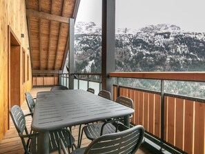Una terraza de madera con mesa y sillas, con vistas a un paisaje montañoso nevado.