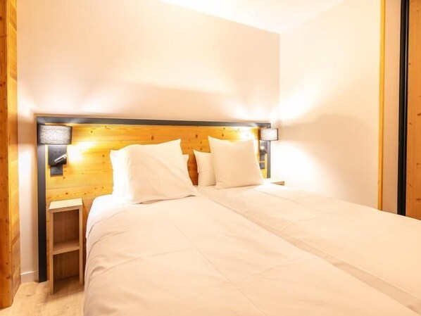 Une chambre à coucher avec une tête de lit en bois, un lit recouvert de linge de lit blanc et une table de chevet avec une lampe.