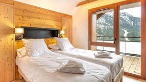 Un dormitorio con paneles de madera, dos camas, un balcón con vista a la montaña y techo de madera.