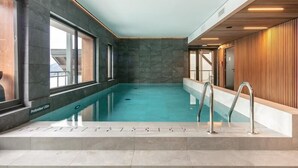 Una piscina interior moderna con agua cristalina, paredes de piedra y un panel de madera en un lateral.