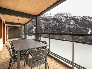 Een overdekt balkon met een tafel en stoelen, met uitzicht op een bergachtig landschap.