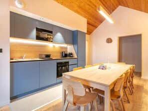 A modern kitchen with grey cabinets, a wooden ceiling, and a dining area with a long table and chairs. - Wifi, 150m from resort center, swimming pool, sauna, hammam, balcony, parking, tv, ski locker, 104m² (Vaujany)