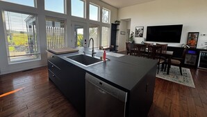 Ett modernt kök med diskmaskin, en matplats med TV och stora fönster.