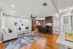 A modern living room with a sofa, coffee table, and a dining area with chairs and a kitchen in the background. - 3-bedroom house in phenomenal Pompano Beach with nice relaxing pool with gazebo (Pompano Beach)
