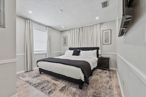 A bedroom with a bed, nightstands, a window with curtains, and a ceiling with recessed lighting.