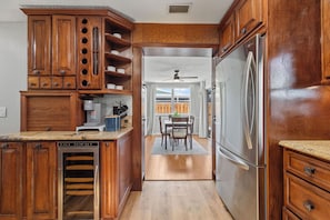 A kitchen with wooden cabinets, a stainless steel refrigerator, a coffee maker, and a dining area with a table and chairs.