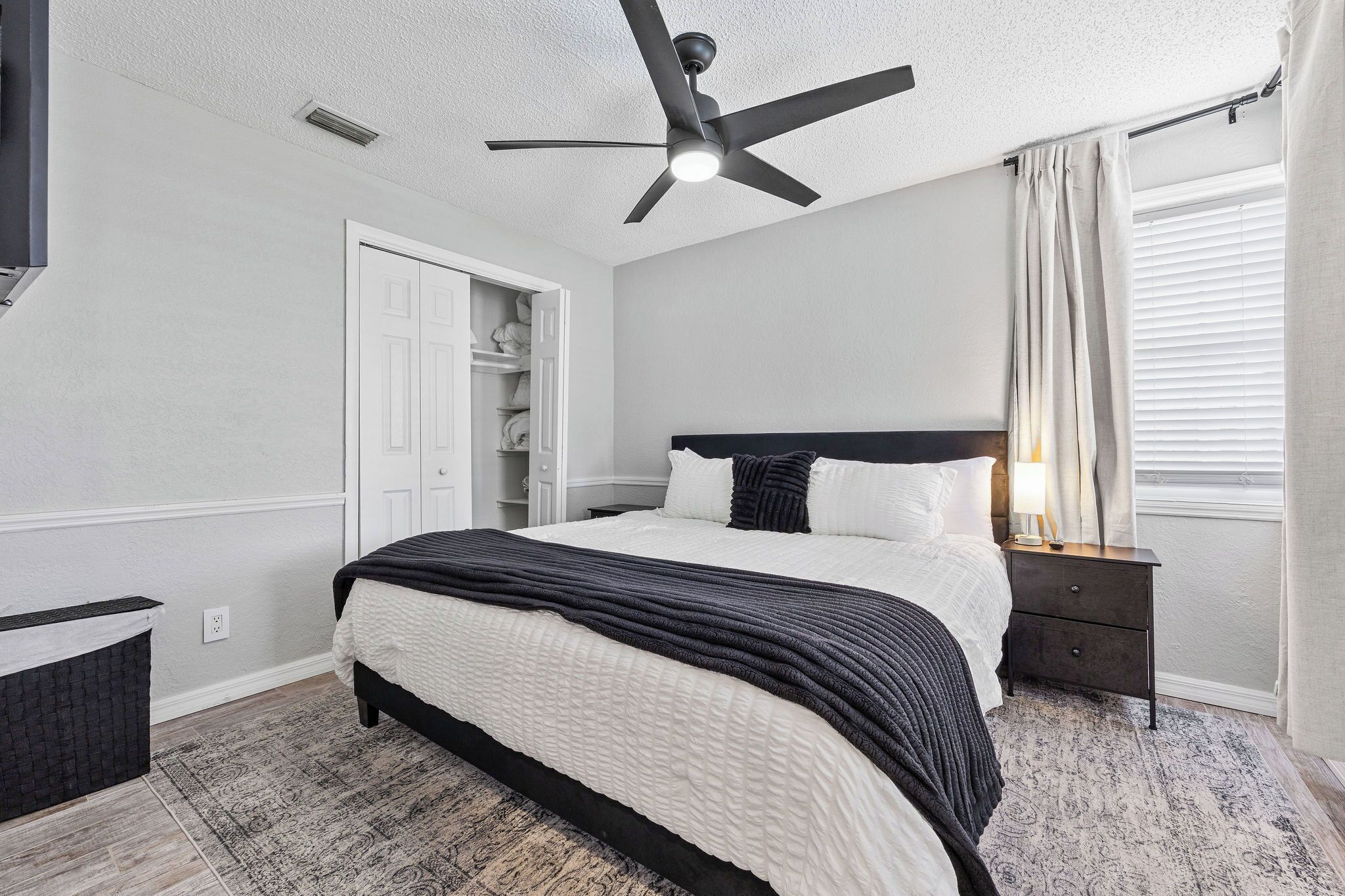 A bedroom with a bed, a nightstand, a ceiling fan, a closet, and a window with curtains.
