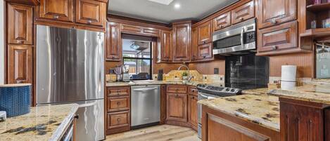 A modern kitchen with wooden cabinets, stainless steel appliances, and a granite countertop.