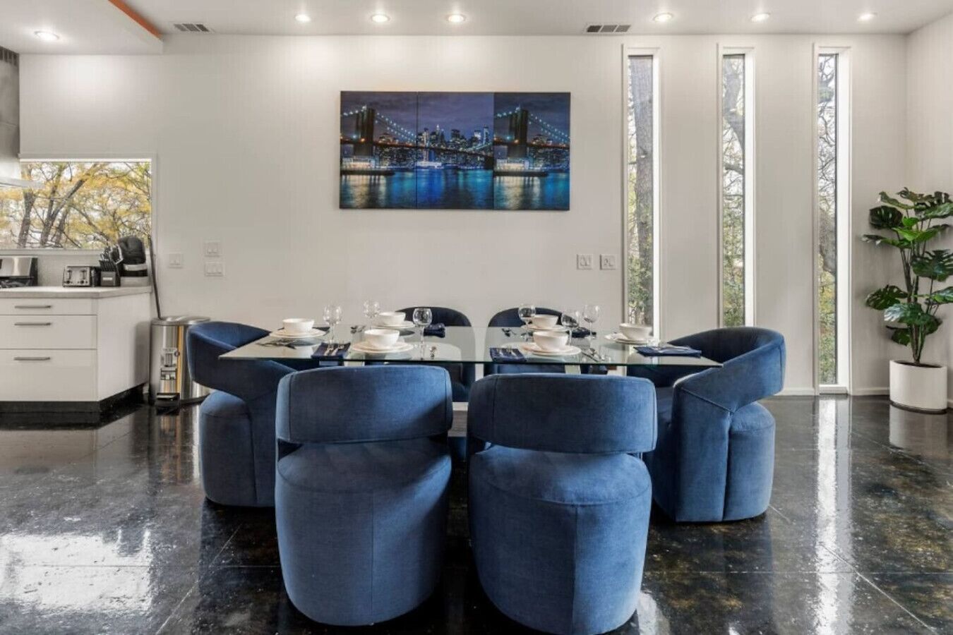 Un espace repas moderne avec une table en verre pour quatre personnes, entourée de chaises à revêtement bleu.