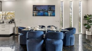 A modern dining area with a glass table set for four, surrounded by blue upholstered chairs. - Modern Retreat Near Atlantic Station (Atlanta)