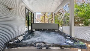 A hot tub with a stone exterior, surrounded by a covered patio with metal siding and large windows. - Modern Retreat Near Atlantic Station (Atlanta)