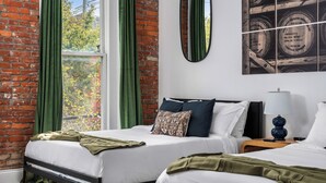Une chambre d’hôtel avec deux lits, des rideaux verts, un mur en briques et une grande fenêtre.