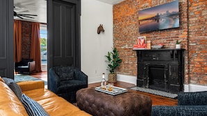Un salon moderne avec des canapés en cuir, un mur en briques, un téléviseur fixé au mur et une cheminée.