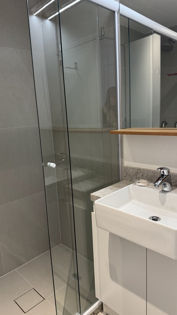 Un baño moderno con cabina de ducha de vidrio, un lavabo blanco y un espejo sobre él.