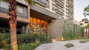 A modern building with a glass facade, outdoor seating area, and a well-maintained garden with palm trees and plants. - Skyline (Porto Alegre)