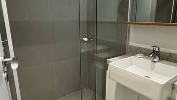 A modern bathroom with a glass shower enclosure, a white sink, and a mirror above the sink.