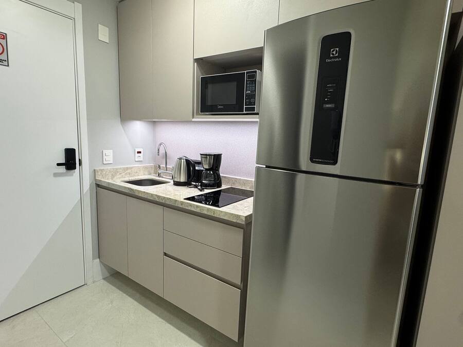 A compact kitchen with a stainless steel refrigerator, a microwave, a coffee maker, and a sink.
