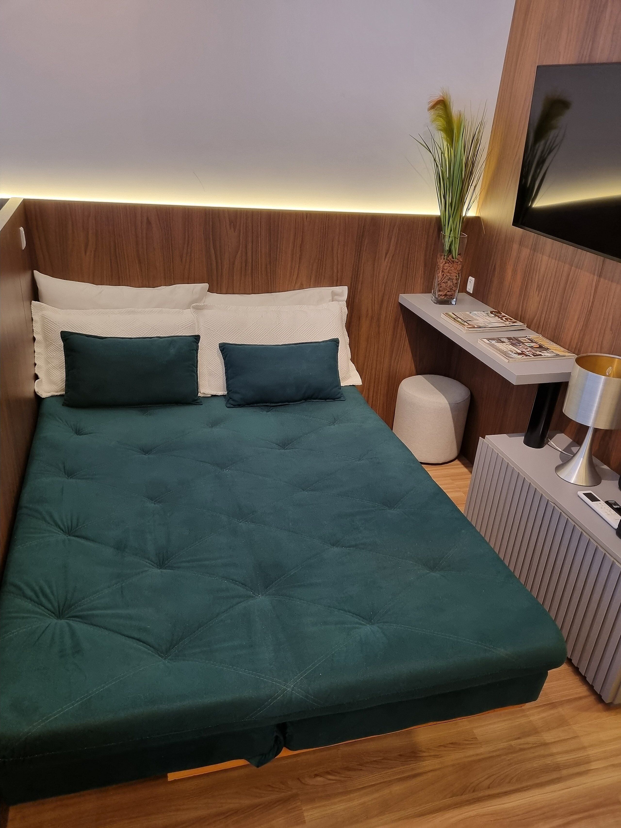 A modern bedroom with a bed, bedside table, lamp, and a TV mounted on the wall.