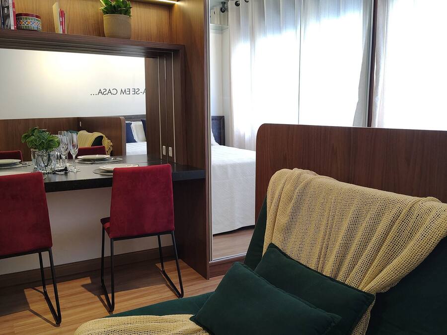 Quarto moderno com cozinha compacta, área de refeições, cama com cortinas e um espaço de estar aconchegante com manta.