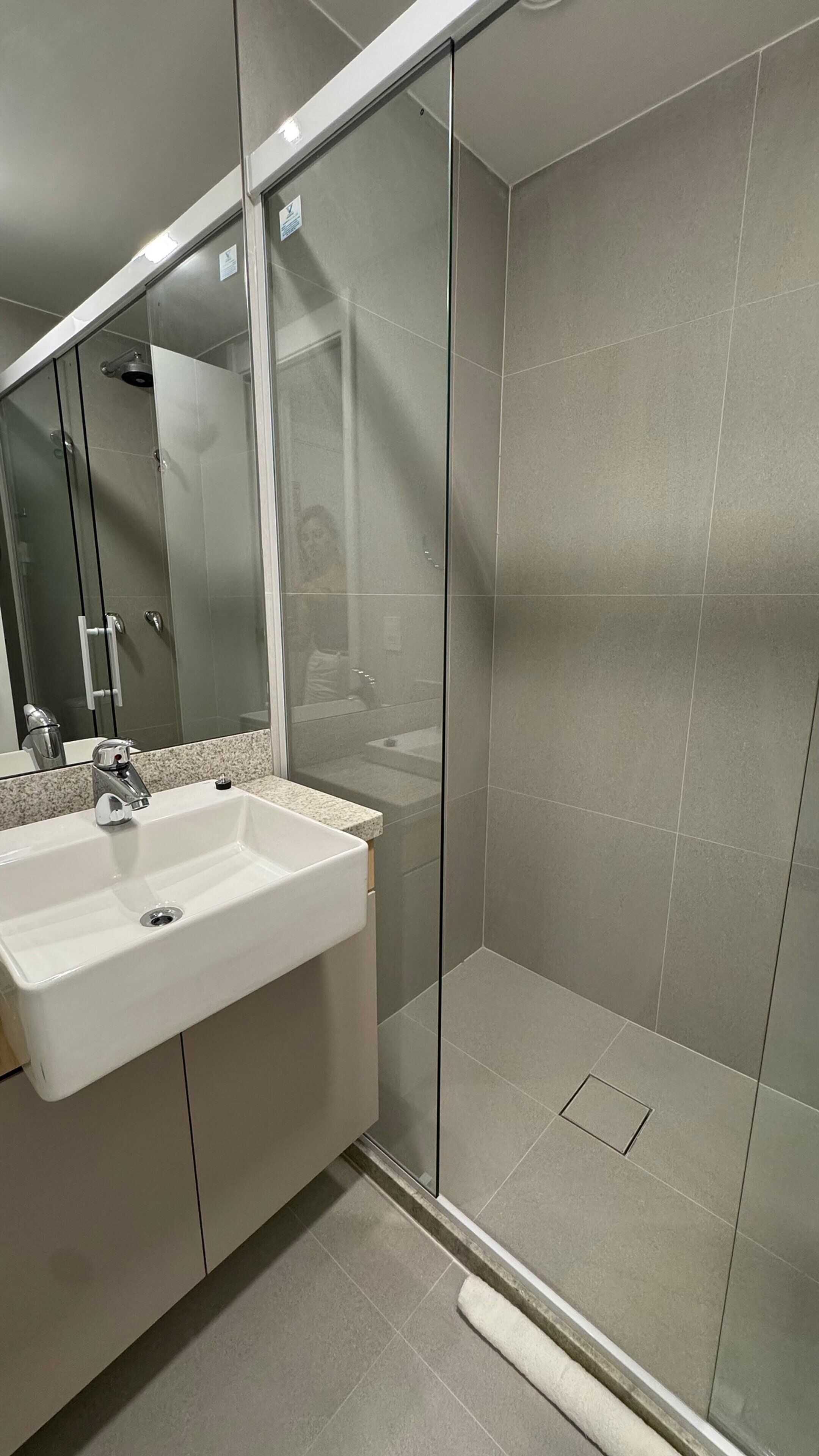 Une salle de bain moderne avec une douche à parois de verre, un lavabo avec un miroir et un sol carrelé.