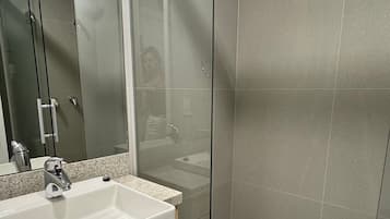 Une salle de bain moderne avec une douche à parois de verre, un lavabo avec un miroir et un sol carrelé.