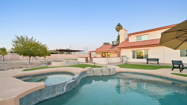 A swimming pool with a curved design, a patio area with a bench, and a house with a red roof.