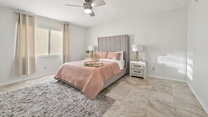 A bedroom with a bed, a nightstand, a lamp, a ceiling fan, and a window with curtains.