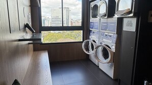 A laundry room with multiple washing machines and dryers, a bench with pillows, and a view of the city through large windows. - GO CARLOS GOMES (Porto Alegre)