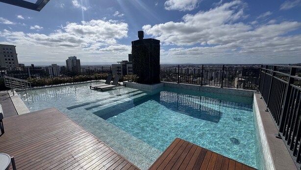 A rooftop infinity pool with clear blue water, surrounded by a wooden deck and lounge chairs. - GO CARLOS GOMES (Porto Alegre)