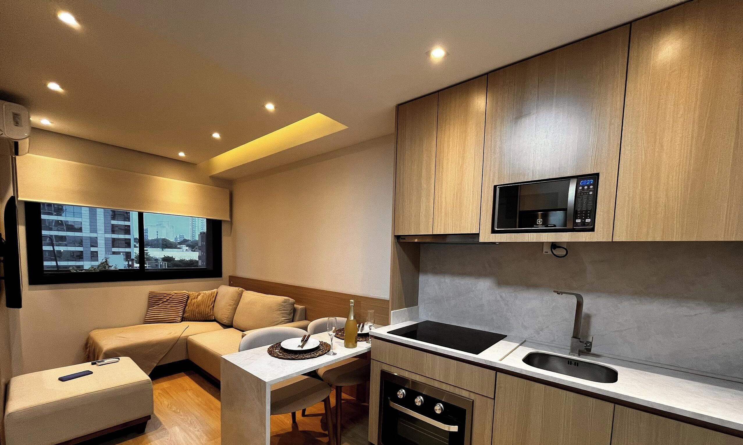 Una cocina compacta con microondas integrado, una zona de comedor con mesa y sillas, y un sofá.