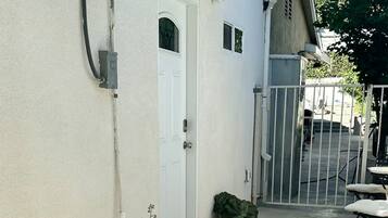 A concrete patio with a white door, a potted plant, and a metal gate.