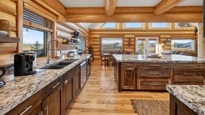 A spacious kitchen with wooden beams, granite countertops, and a large island. - Here & Now | Luxe Yellowstone Cabin w/ Hot Tub & Views! (Island Park)
