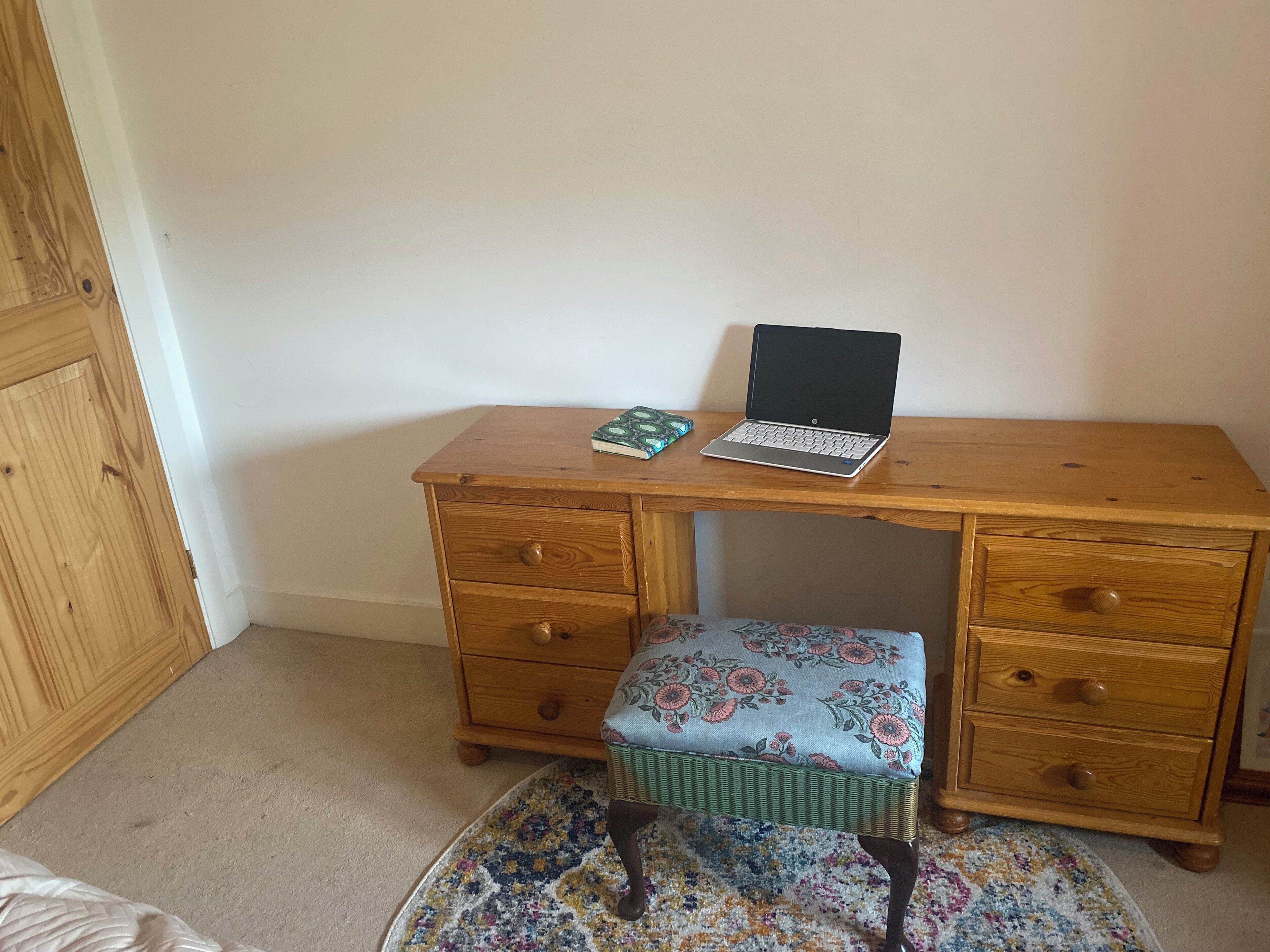 Un bureau en bois avec un ordinateur portable, un carnet et un coussin à motifs.
